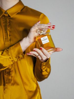 Classy woman in a gold silk shirt holding a luxury perfume in Paris.