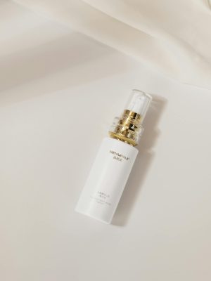 Elegant white skincare bottle with gold accents lying on a soft cream background, suggesting luxury and sophistication.
